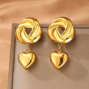 Polished gold twisted knot earrings with hanging 3D heart charms on a silk background