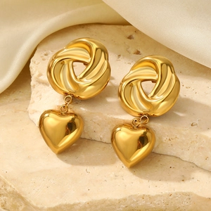 Detail of gold spiral knot heart drop earrings on a natural stone and silk background