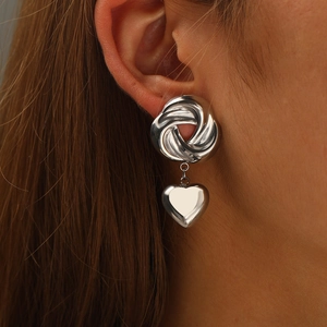 Detailed view of silver heart pendant earrings on model with spiral knot and glossy finish