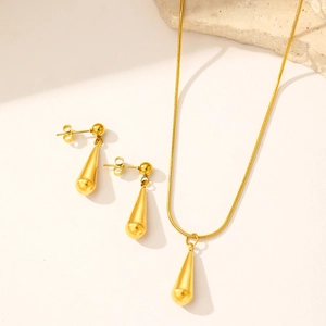 Polished gold teardrop jewelry set with necklace and earrings on a textured stone
