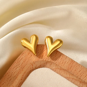 Detailed view of luxury gold heart stud earrings on a beige linen jewelry display stand