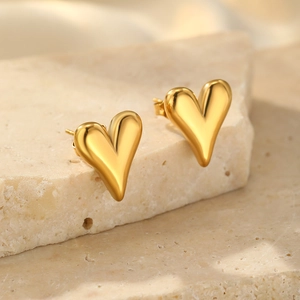 Macro view of gold heart stud earrings with a glossy finish on a stone display tray