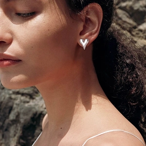 Close-up of heart-shaped silver stud earring on ear with polished metallic finish