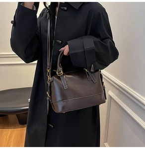 Detailed shot of dark brown glossy leather bag with white stitching and gold hardware