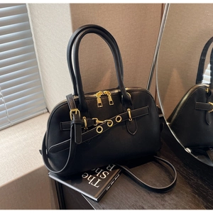 Close-up of black leather Boston bag with decorative gold eyelet buckles and crossbody strap