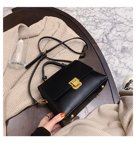 Detail der schwarzen Handtasche aus Leder mit goldenem Drehverschluss und Bodenfüßen