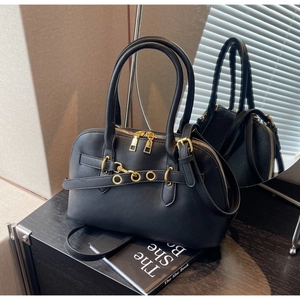 Detail of black textured leather handbag with gold hardware and dual zippers on a desk