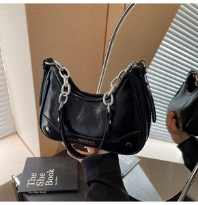 Detail of glossy black patent leather bag with thick silver chain and metal logo