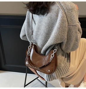 Detail of glossy brown underarm bag featuring a silver chain and luxury leather texture