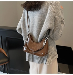 Detail of glossy brown patent leather hobo bag with thick silver chain and logo