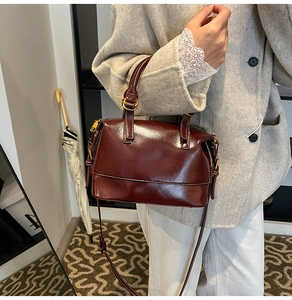 Detail einer glänzenden tiefroten Boston Bag mit goldenen Beschlägen und feiner Lederoptik