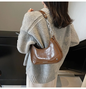 Close-up of brown semi-circle leather underarm bag with silver chain and rivets