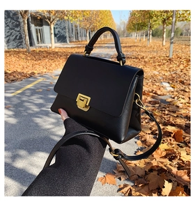 Detail of a black leather crossbody bag with golden rectangular lock and pebble texture