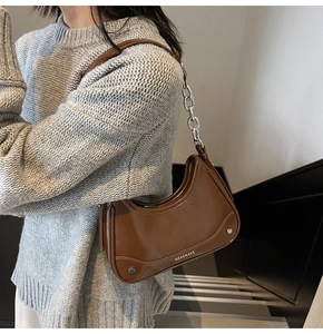 Close-up of caramel brown underarm bag with silver chain and logo detail on gray sweater