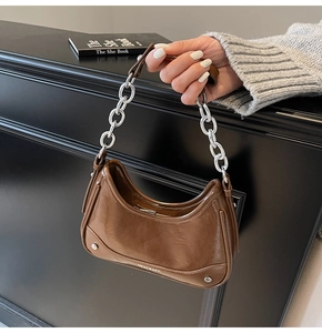 Detail of a brown crescent-shaped bag featuring a silver metal chain and glossy texture