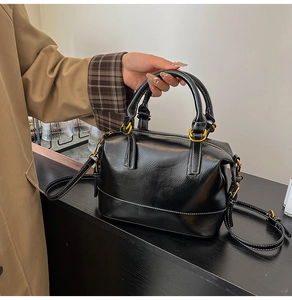 Details der schwarzen Boston-Tasche aus Ölwachsleder mit weißen Kontrastnähten und Goldteilen