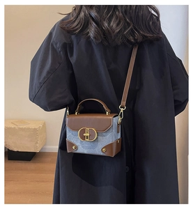 Detail of blue denim and brown leather crossbody bag with a gold twist lock closure