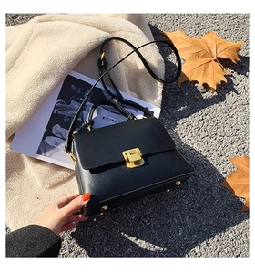 Détail d'un sac à main en cuir noir avec fermoir doré posé sur des feuilles d'automne