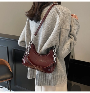 Detail of burgundy patent leather underarm bag featuring a chunky silver metal chain
