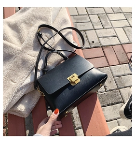 Detail einer schwarzen Handtasche aus Leder mit Lychee-Struktur und goldener Schließe