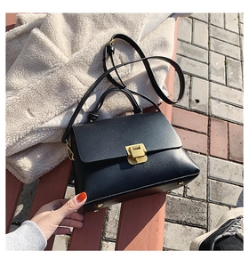 Detailansicht einer schwarzen Lederhandtasche mit goldenem Druckverschluss auf einer Bank