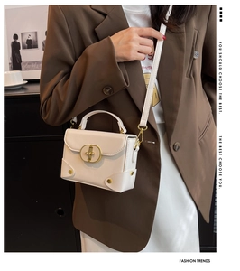Detailed view of white structured handbag with golden twist lock on a shoulder strap