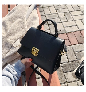 Close-up of black leather trapezoid bag with metallic gold square lock on a wooden bench