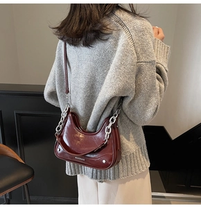 Detailed shot of burgundy crescent shoulder bag with glossy finish and silver chain strap