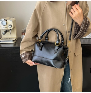 Detail of glossy black leather tote bag with vintage gold hardware on khaki trench coat