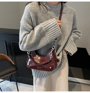 Detail of burgundy patent leather half-moon shoulder bag with silver chain and strap
