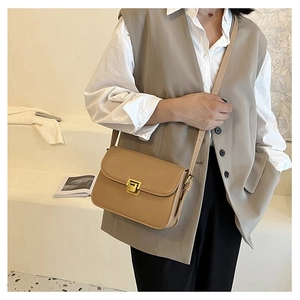 Close-up of khaki leather crossbody bag with a gold twist-lock on a fashion model