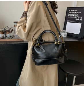 Detail of a black leather Boston bag with white stitching and gold hardware on a cafe table