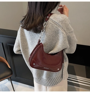 Detail of burgundy glossy half-moon bag featuring silver chain strap and metal rivet accents