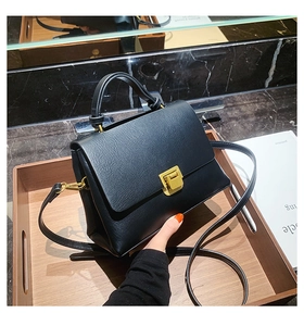 Detail of elegant black matte leather handbag with square gold metal clasp and top handle