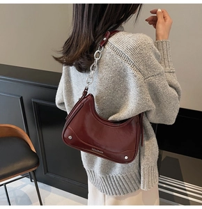 Close-up of dark burgundy crescent shoulder bag with glossy leather and silver chain