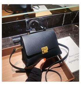 Détail d'un sac à main noir en similicuir avec fermoir doré sur un plateau en bois