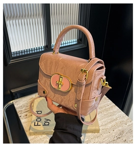 Close-up of pink textured crossbody bag with gold oval lock and elegant pleated detail