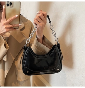 Detail of black patent leather crescent bag with silver chain strap and metal rivet studs