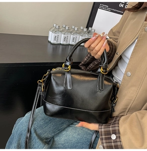 Detail der schwarzen Boston-Tasche aus Wachsleder mit weißen Nähten und Goldbeschlägen