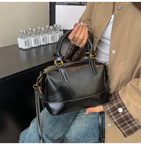 Detailed close-up of a glossy black leather Boston bag with white contrast stitching and gold rings