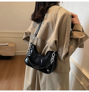 Détail d'un sac demi-lune en cuir brillant noir avec chaîne en métal argenté et sangle