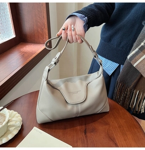 Close-up of litchi grain leather texture and embossed logo on beige shoulder bag