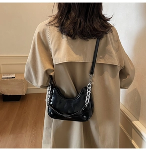 Detail of black patent leather hobo bag with silver chain strap and branding on side