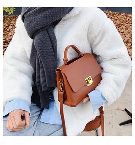 Close-up of a retro caramel leather crossbody bag with gold buckle on a fuzzy white coat