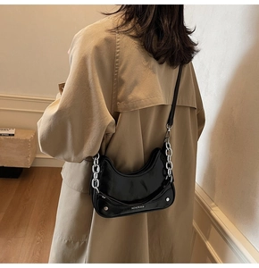 Detail of a black glossy half-moon underarm bag with silver chain on a beige trench coat