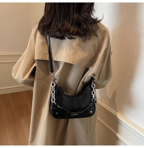 Détail du sac demi-lune en cuir verni noir avec chaîne argentée et logo embossé