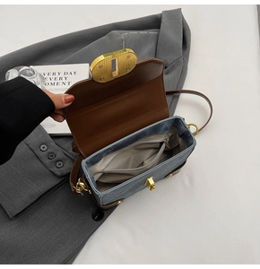 Detail of denim crossbody bag with brown leather trim, interior pocket and gold lock
