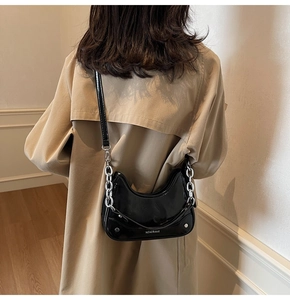 Detailed view of black patent leather hobo bag with silver chain strap on trench coat
