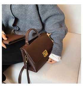 Détail du sac à main en cuir marron avec fermoir doré sur un canapé texturé