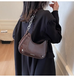 Detail of dark brown crescent bag with glossy leather texture and bold silver chain strap